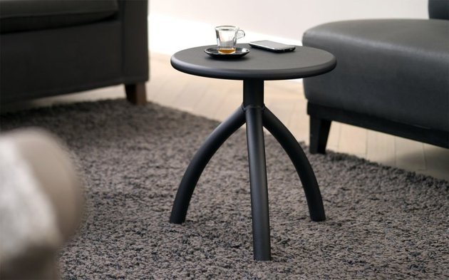 Versão preta da peça usada como mesa de canto ao lado de um sofá escuro