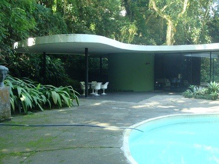 Casa das Canoas, no Rio de Janeiro, com laje branca de formas curvas sobre pavilhão de vidro, cercada de árvores, ao lado de uma piscina