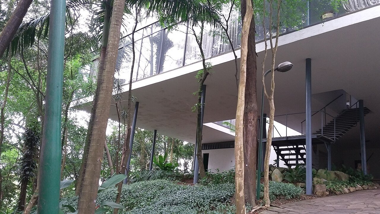 Casa de Vidro, em São Paulo, com o andar de vidro apoiado em pilotis finos entre palmeiras e árvores altas da Mata Atlântica