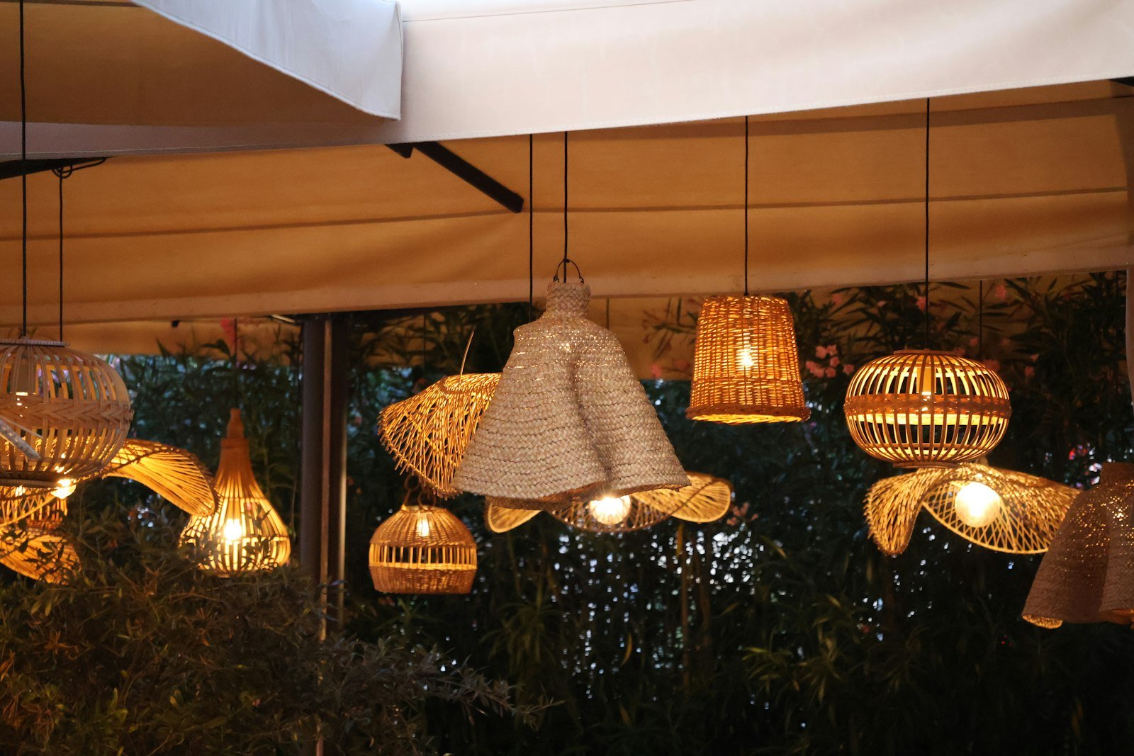 Luminárias de palha trançada penduradas sob uma cobertura, sobre plantas tropicais