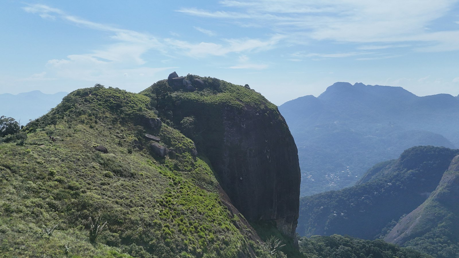 Pico de montanha com paredão de pedra e encosta coberta de mata