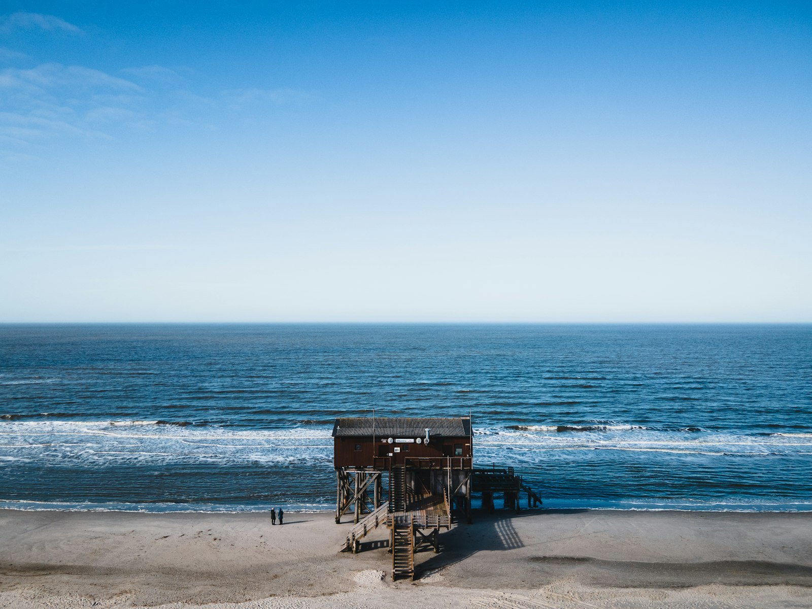 Casa de madeira sobre palafitas numa praia, com ondas ao fundo