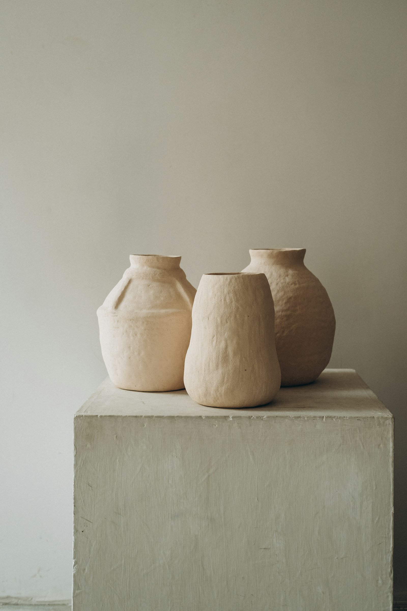 Três vasos de barro marrom sobre uma mesa de concreto branco