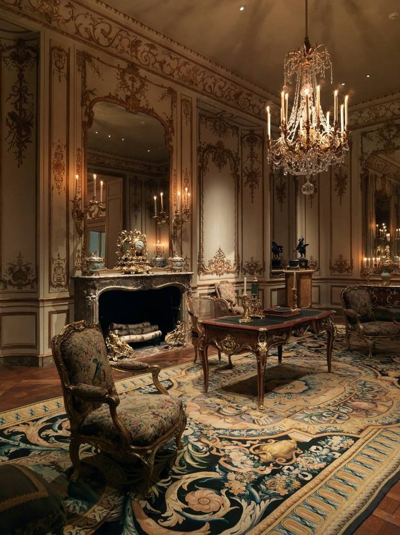 Salão com lustre de cristal, painéis claros nas paredes, poltronas de época e tapete estampado