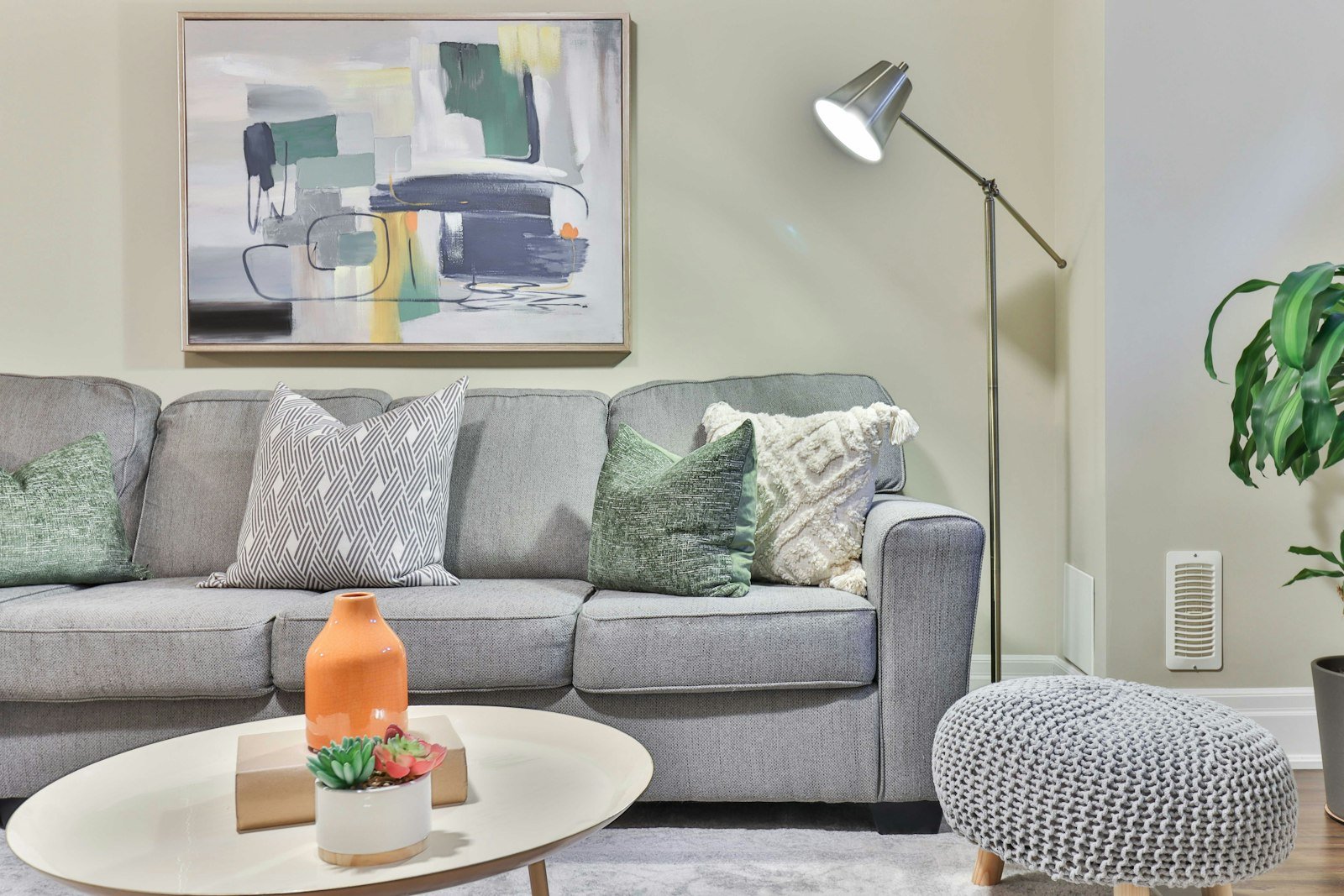 Sala com sofá cinza, almofadas, quadros na parede e luminária de piso