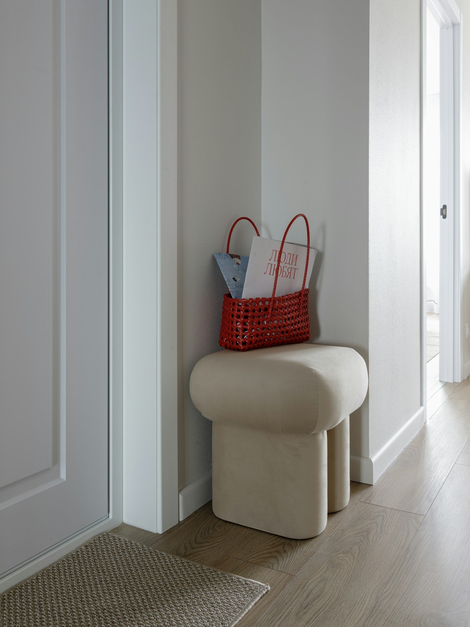 Cesto de fibra com revistas sobre banqueta estofada bege em um corredor